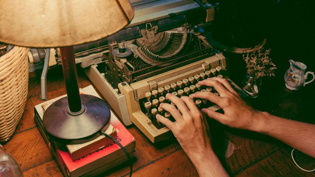 Hands typing on a vintage typewriter under a warm lamp glow, evoking nostalgia.