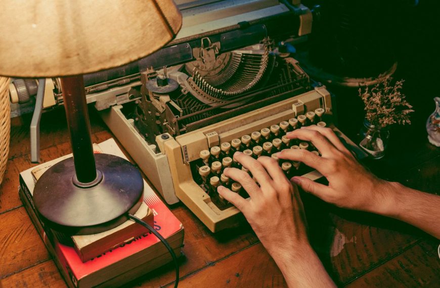 Hands typing on a vintage typewriter under a warm lamp glow, evoking nostalgia.