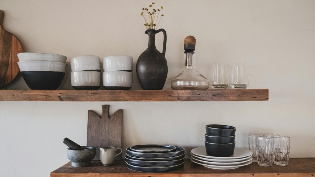 Stylish arrangement of ceramic bowls and glassware on rustic wooden shelves.