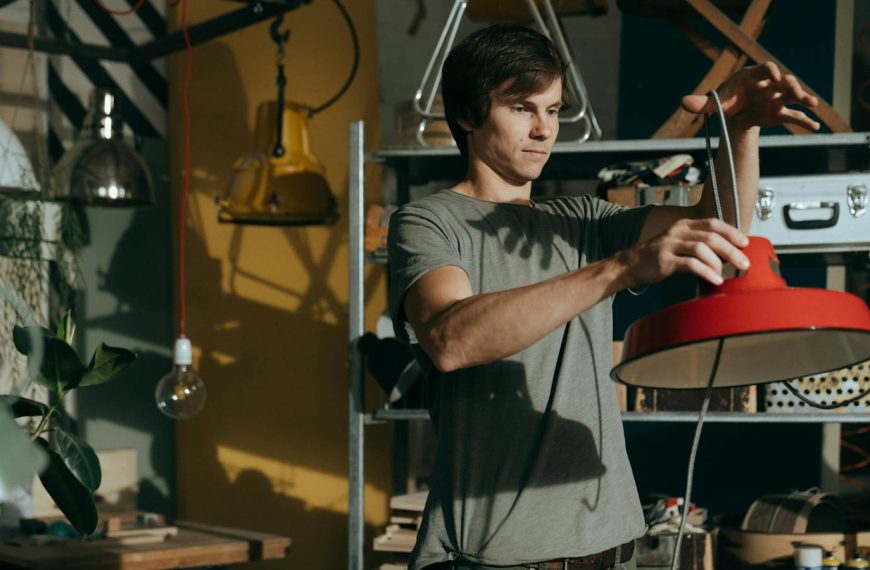 A man working indoors repairing a red lamp in a craft workshop environment.