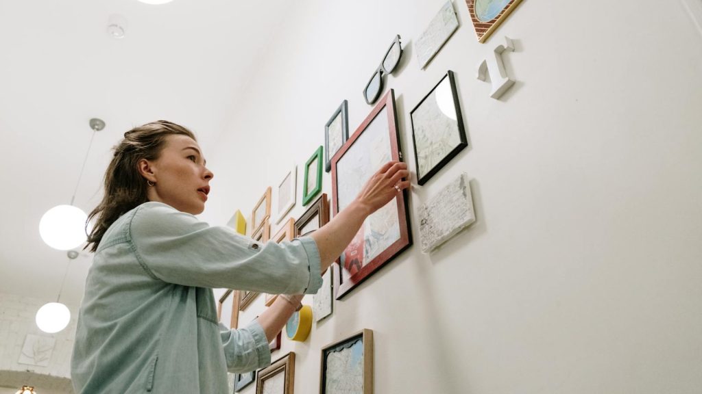 A woman arranging picture frames on a bright indoor wall.