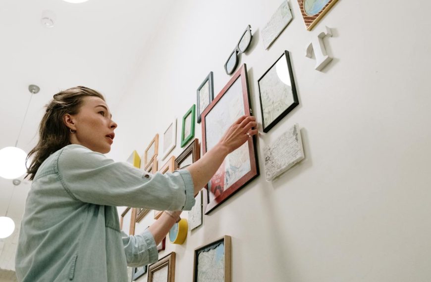 A woman arranging picture frames on a bright indoor wall.