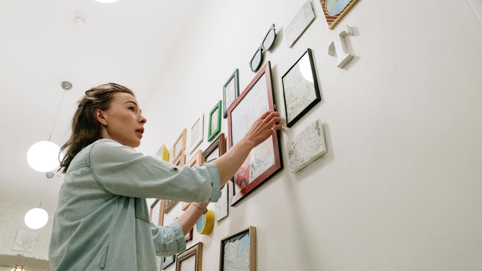 A woman arranging picture frames on a bright indoor wall.
