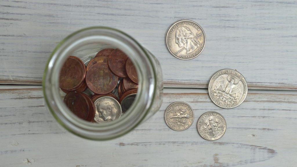 Top view of a jar filled with coins placed on a wooden table, depicting savings.