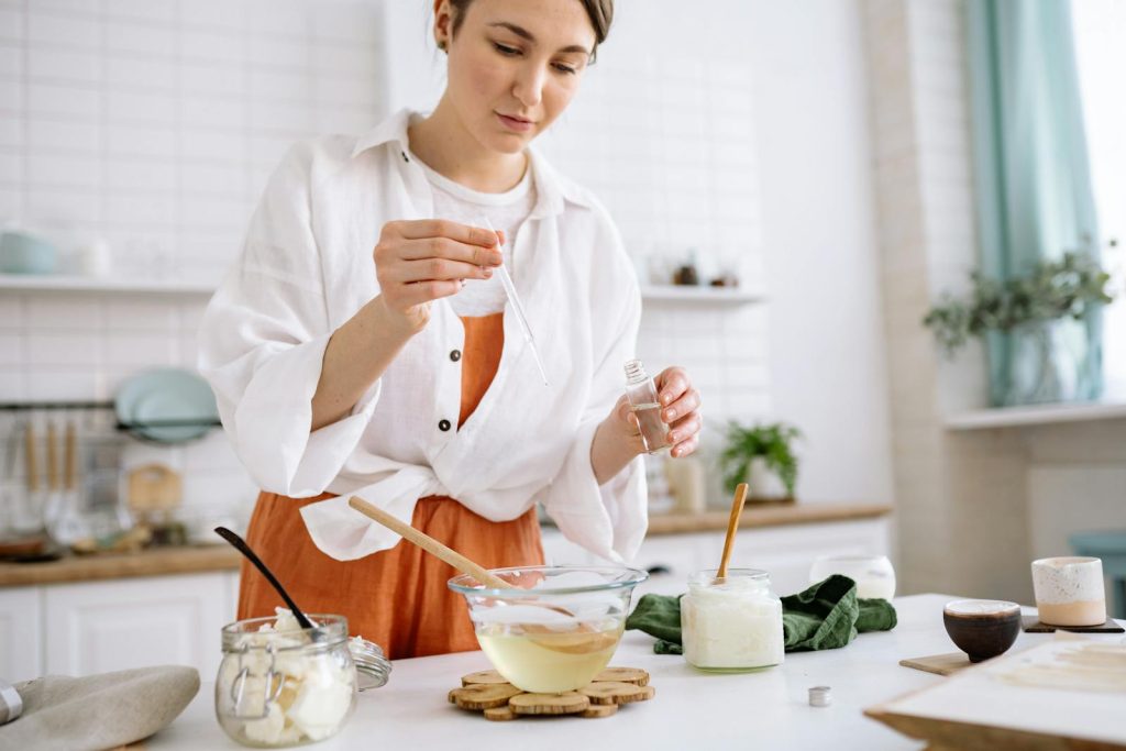 A woman uses a dropper to craft homemade candles in a cozy kitchen setting.