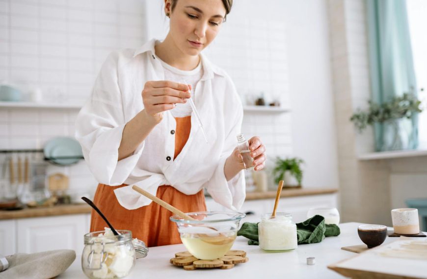 A woman uses a dropper to craft homemade candles in a cozy kitchen setting.