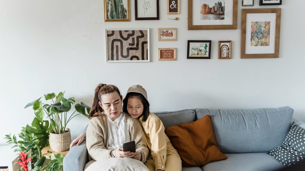 Mother and daughter sitting together on a couch, surrounded by framed art and plants.