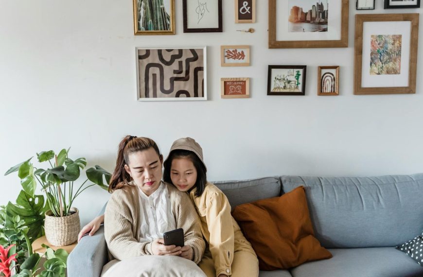 Mother and daughter sitting together on a couch, surrounded by framed art and plants.