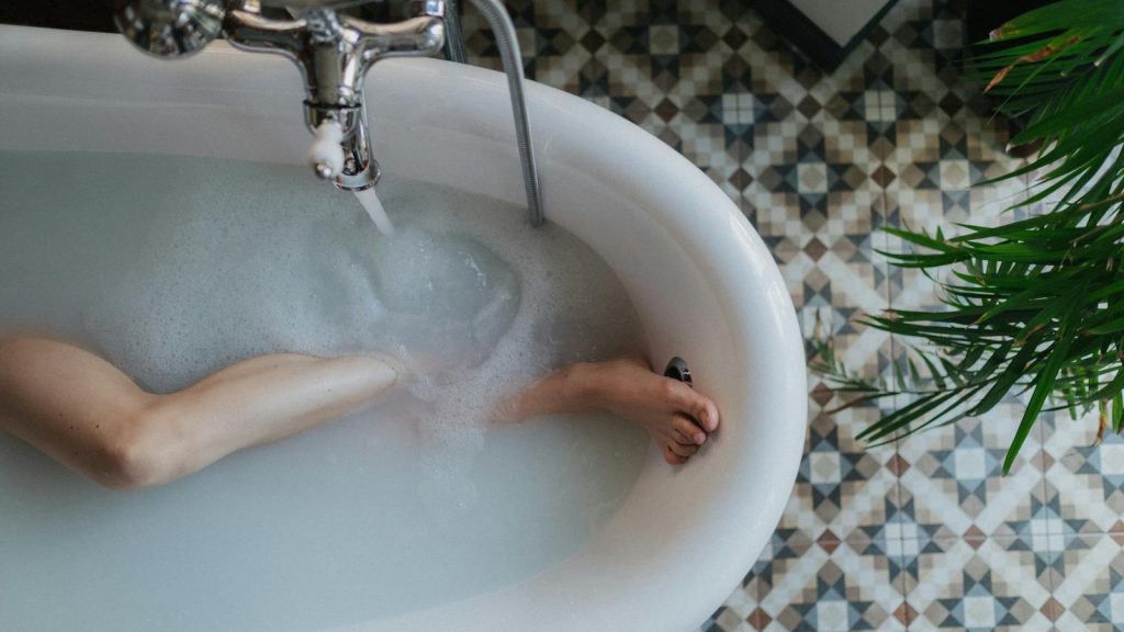 Top-down view of a bathtub with foam, a relaxing foot soaking moment, and stylish floor tiles.