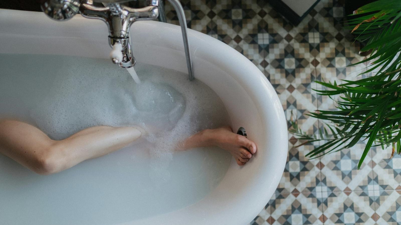 Top-down view of a bathtub with foam, a relaxing foot soaking moment, and stylish floor tiles.