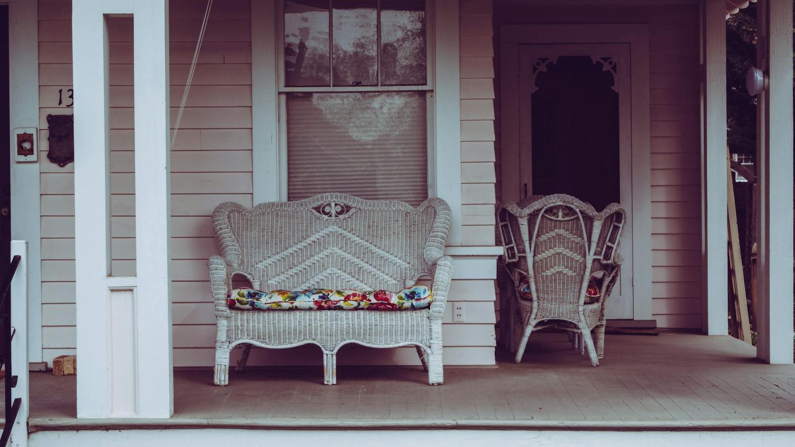 Cozy vintage-style front porch with white wicker chairs and floral cushions.