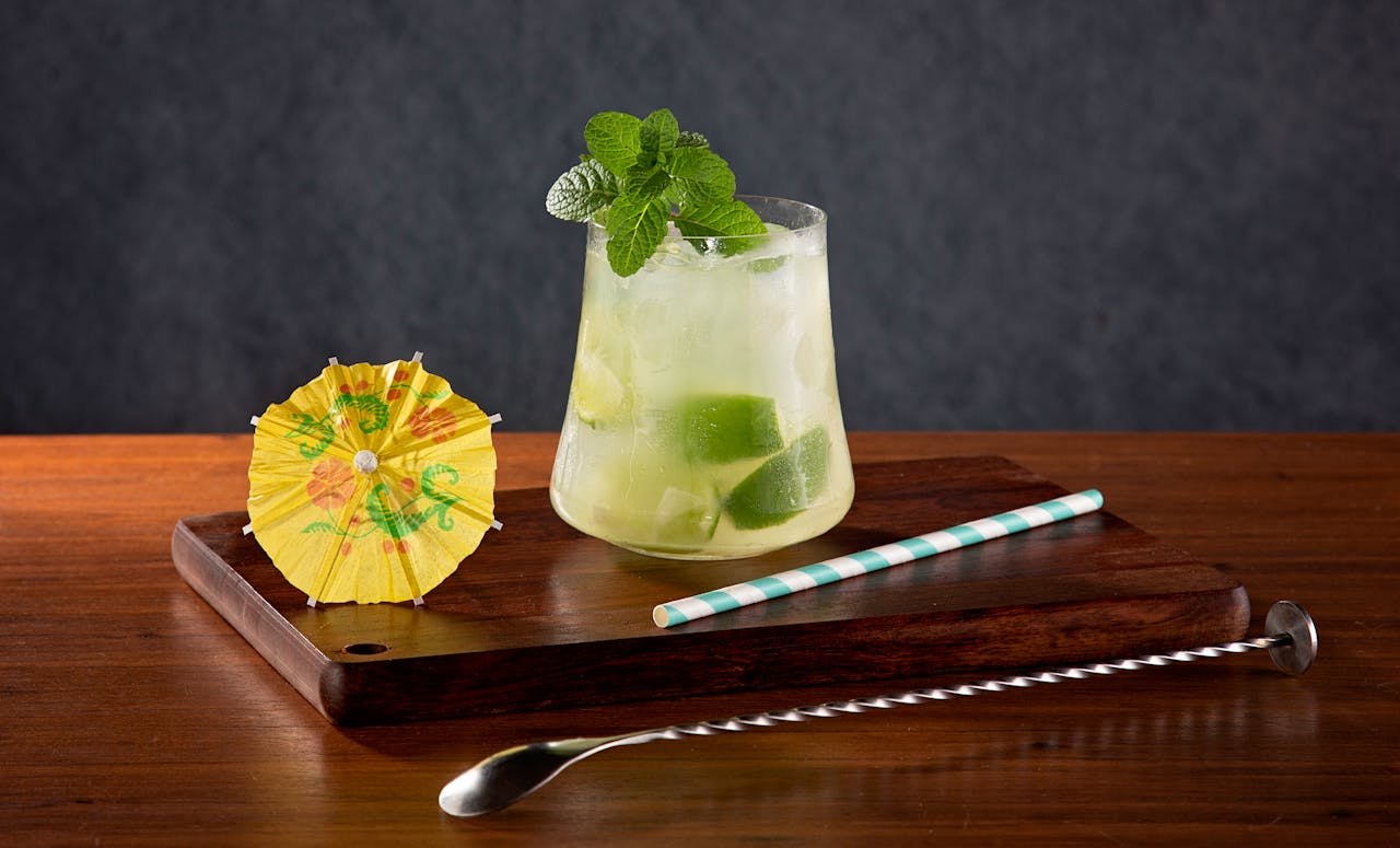 A cocktail with a straw and a spoon on a wooden tray