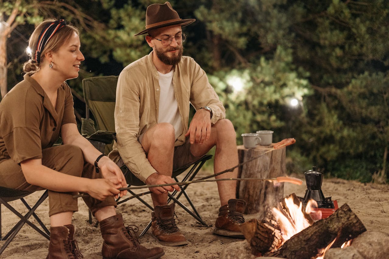 Man and Woman Sitting on Folding Chairs and Grilling Sausages over the Fire