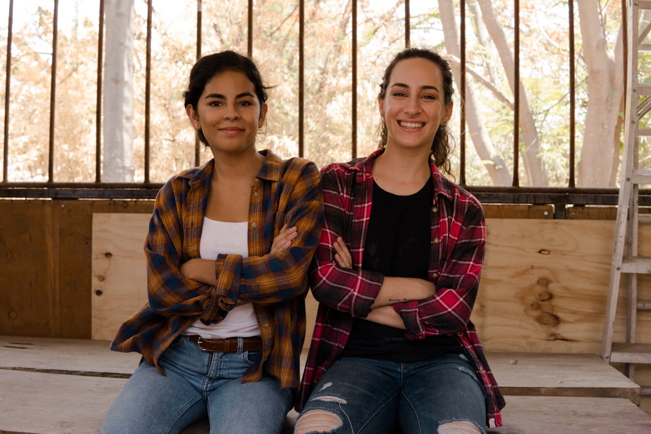 Two Women Wearing Plaid Dress Shirt and Denim Jeans Sitting on Wooden Table
