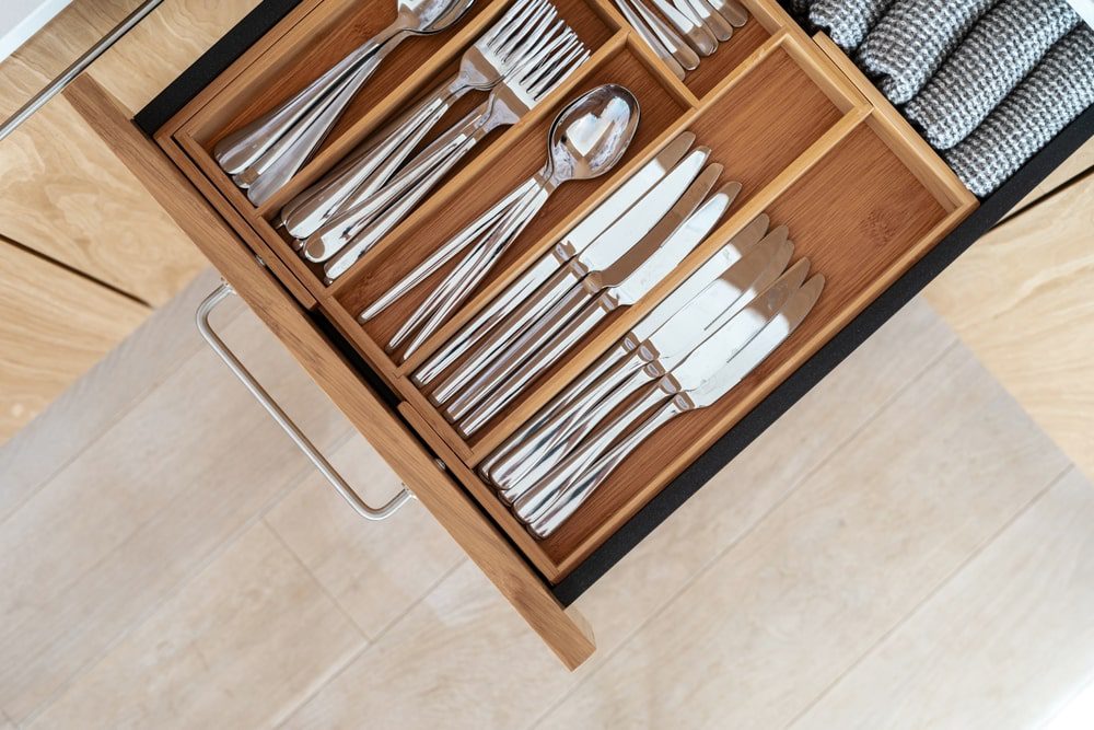 Top view of cutlery set in bamboo trays in kitchen drawer. Keeping steel spoons, knives, forks and other utensilin organizer box with minimalist order. Modern storage idea