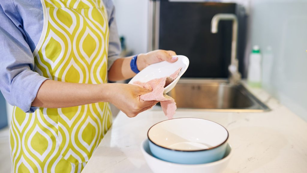 Cropped image of housewife in apron wiping clean dishes with soft cloth hand cleaning