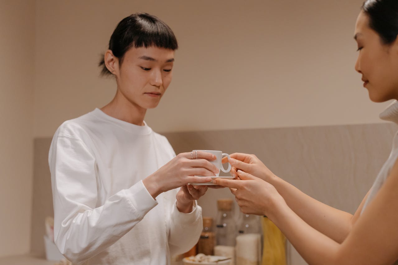 Ethnic mother giving coffee cup to teenage daughter in kitchen
