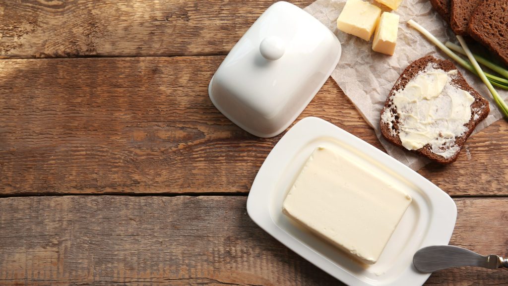 Piece of butter in dish, knife and delicious toast on wooden table