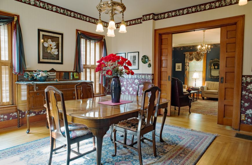 Victorian dining room with wallpaper, high ceiling, silver chandelier, oriential rug & Queen Anne table, chairs & buffet in old home with pocket doors.