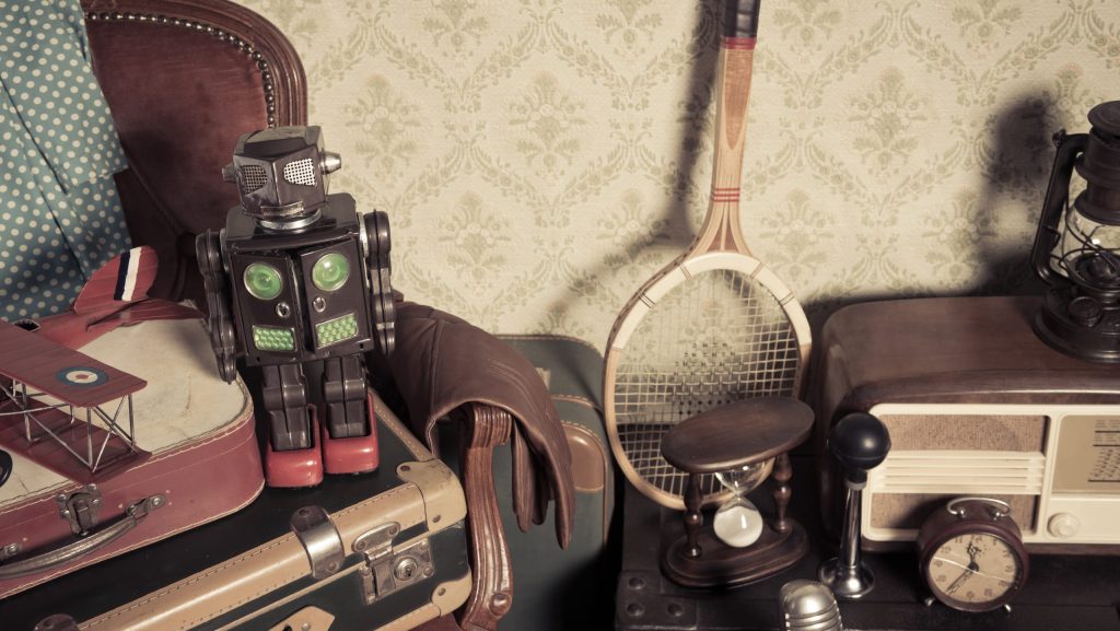 Group of vintage assorted items on attic hardwood floor with vintage wallpaper background.