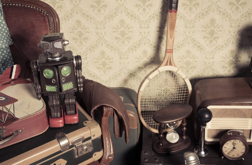 Group of vintage assorted items on attic hardwood floor with vintage wallpaper background.