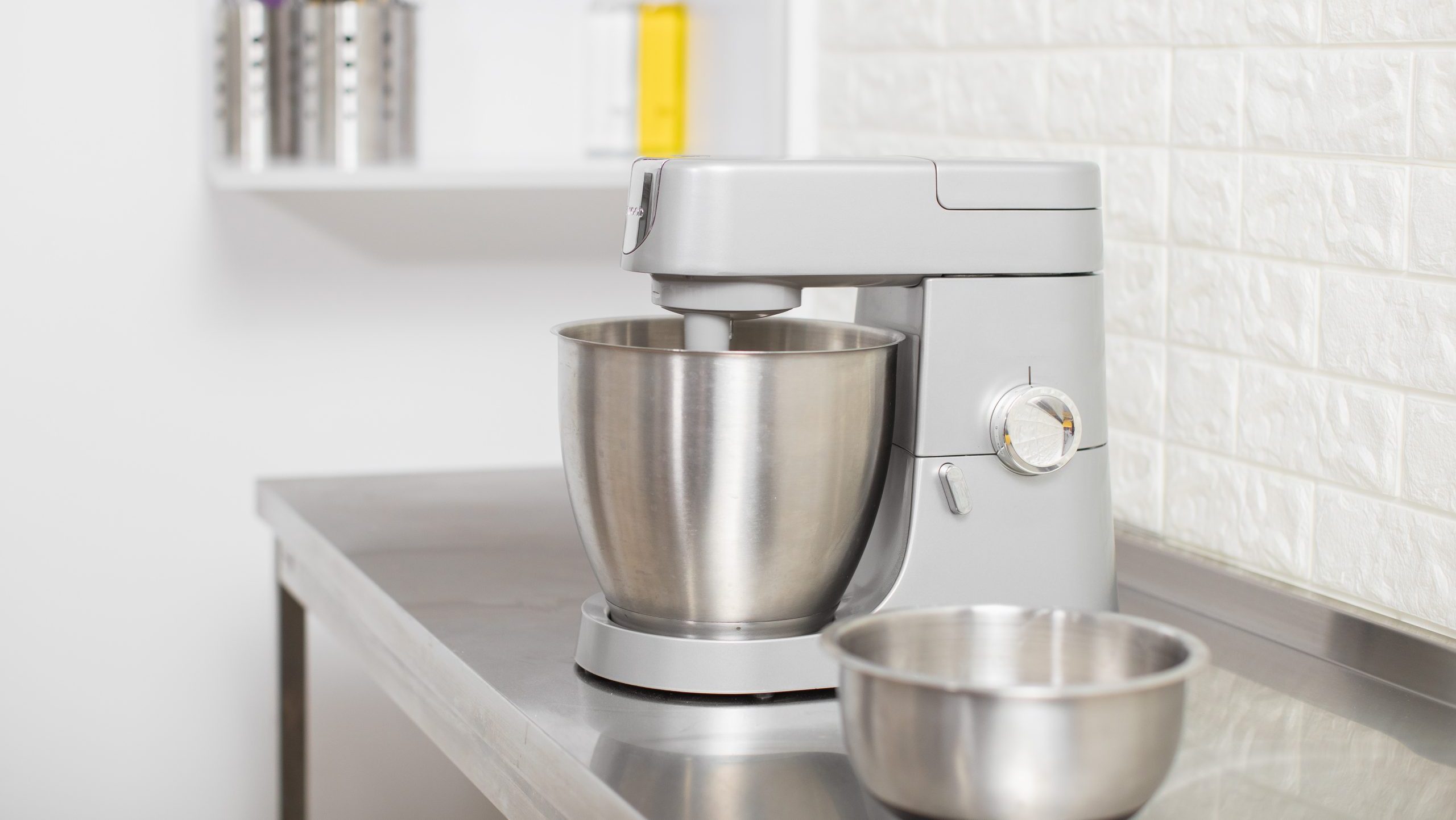 Small Electric Kitchen Appliances. Modern silver kitchen stand mixer in light cozy confectionery. A closeup of Multi-Task Blender mixing dough, and Stainless Steel bowl on the table