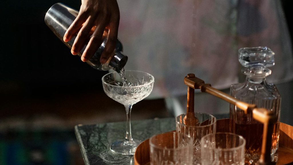 A bartender pours a cocktail into a glass from a shaker, set in a cozy home bar.
