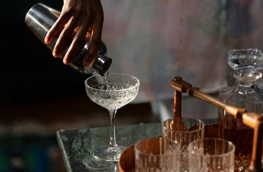 A bartender pours a cocktail into a glass from a shaker, set in a cozy home bar.