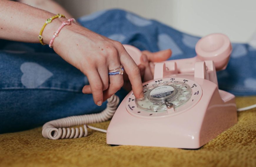 Close-up of a person dialing on a pink rotary phone, evoking a sense of nostalgia and retro charm.