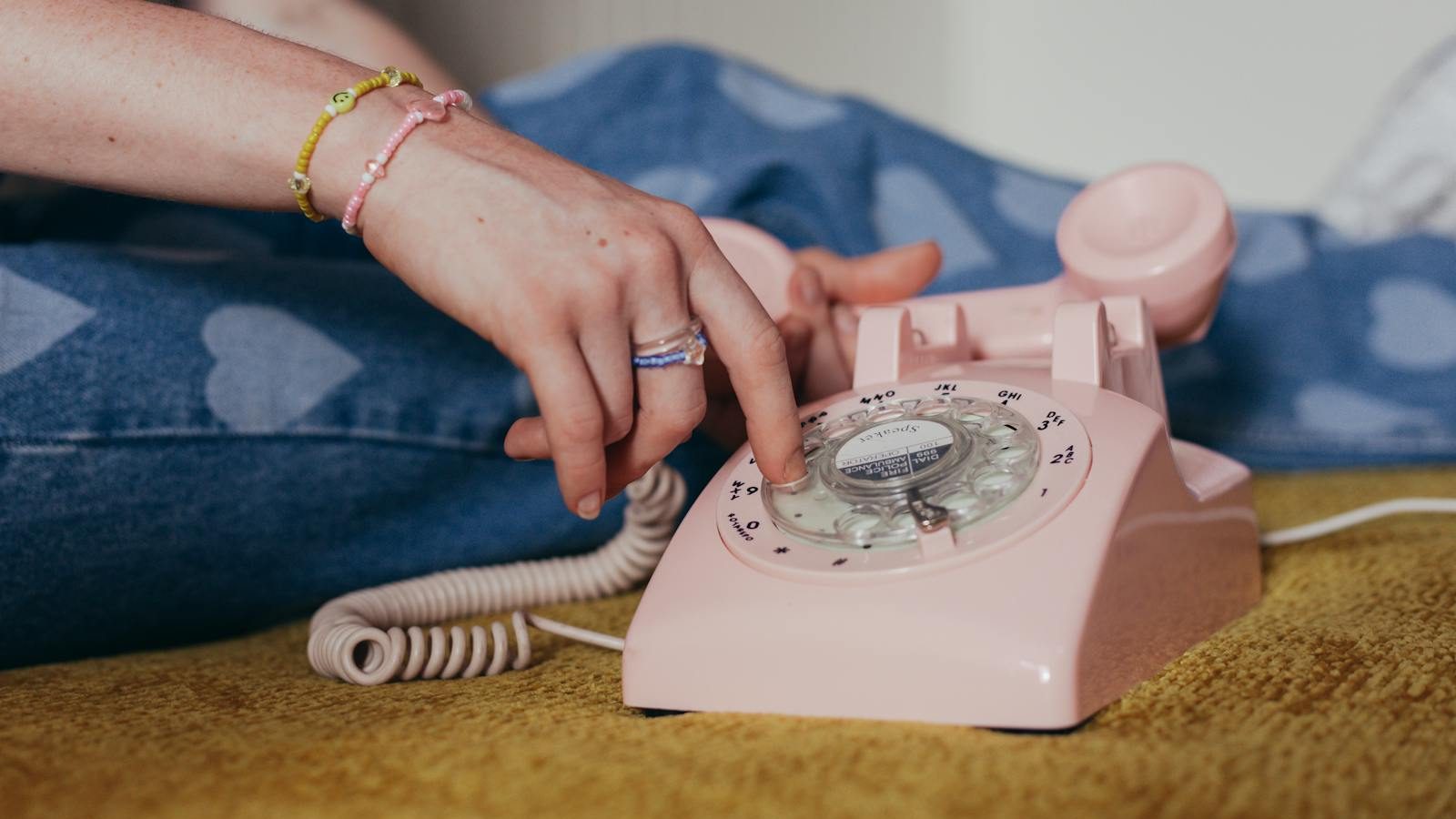 Close-up of a person dialing on a pink rotary phone, evoking a sense of nostalgia and retro charm.