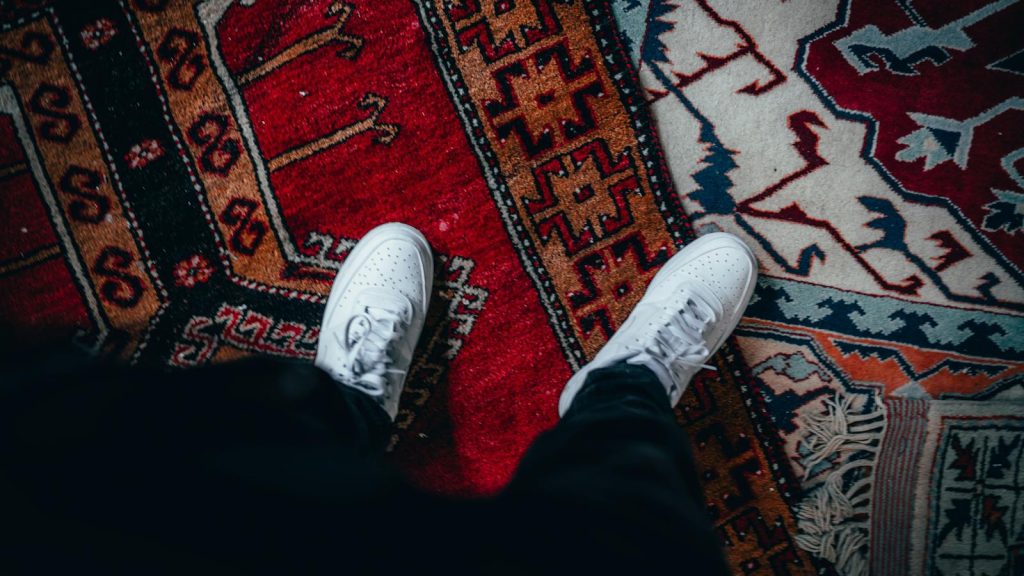 Top view of white sneakers on a colorful patterned rug, emphasizing style and indoors setting.