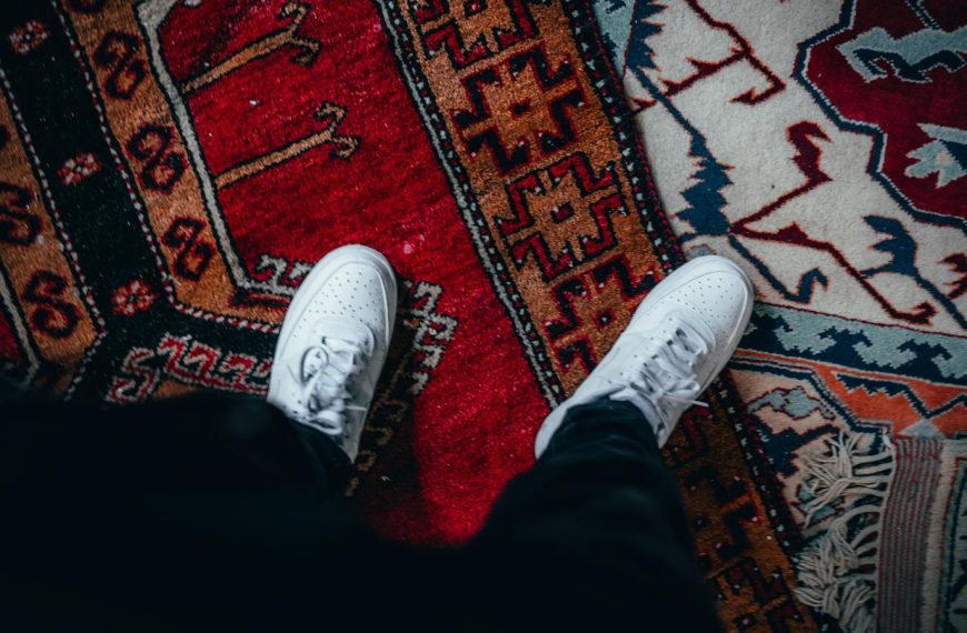 Top view of white sneakers on a colorful patterned rug, emphasizing style and indoors setting.