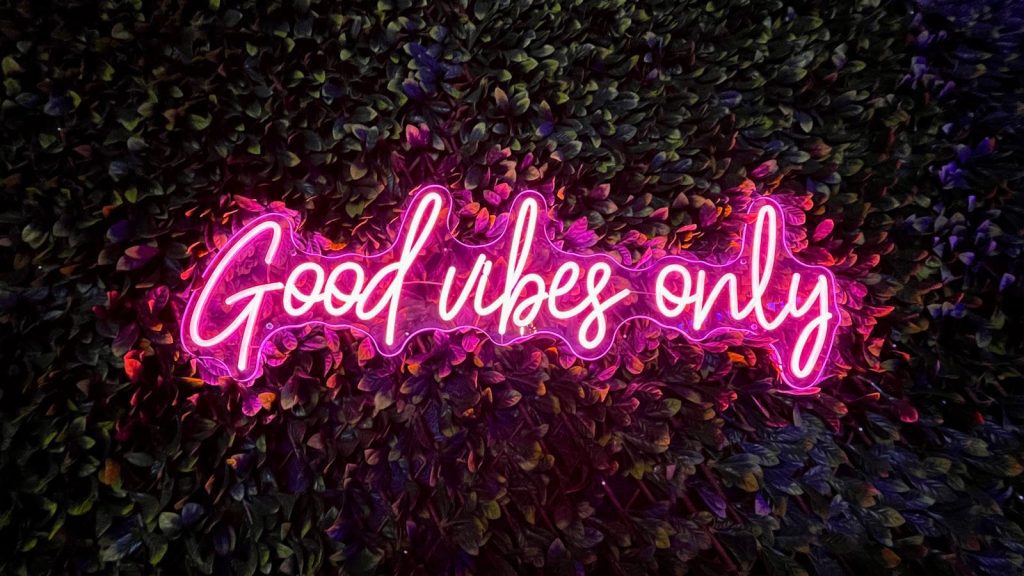 Vibrant pink neon sign reading 'Good vibes only' against a lush leafy wall.