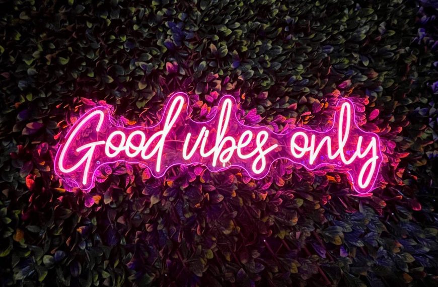 Vibrant pink neon sign reading 'Good vibes only' against a lush leafy wall.