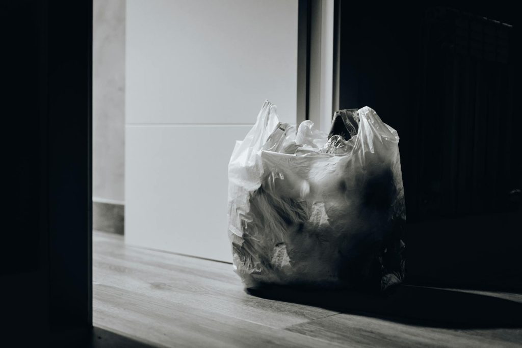 A dimly lit room containing a plastic bag filled with trash, emphasizing waste and recycling.
