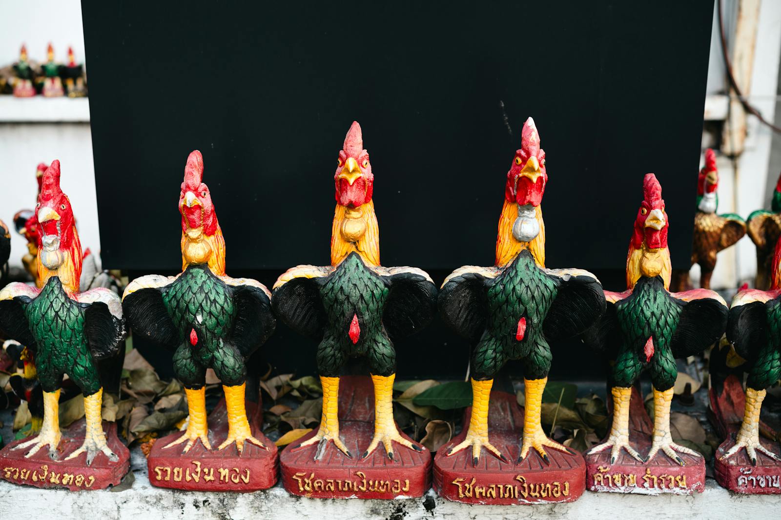 Row of vibrant handmade rooster figurines with decorative Thai inscriptions.