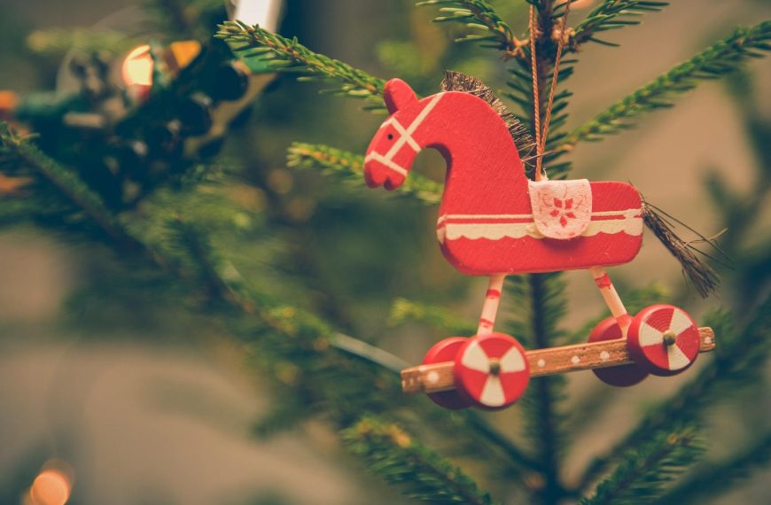 Close-up of vintage wooden horse ornament hanging on a festive Christmas tree branch.
