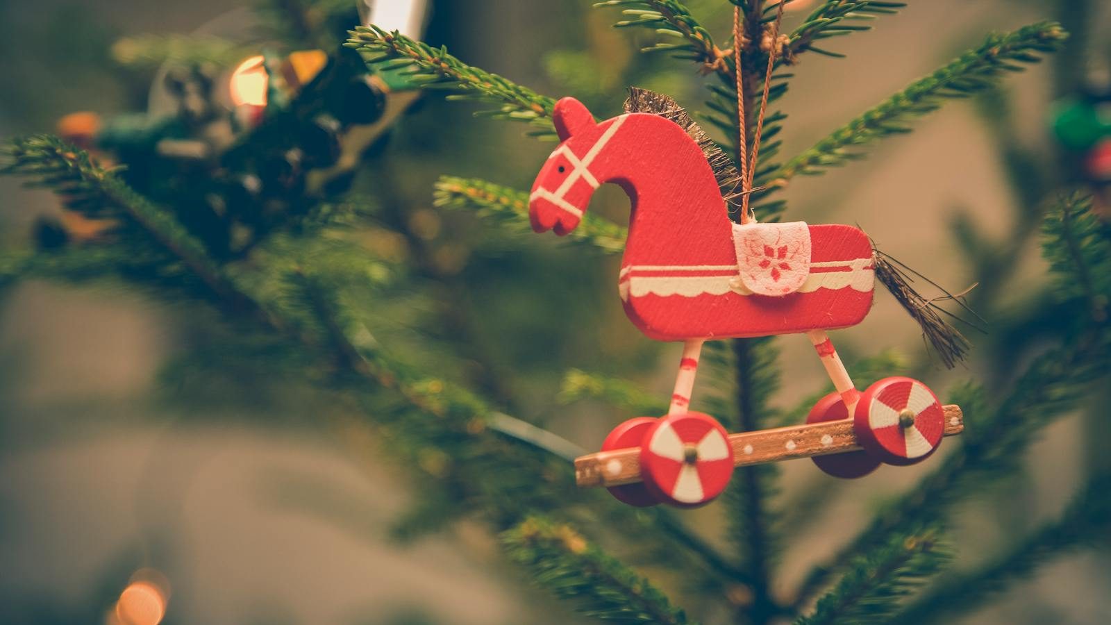 Close-up of vintage wooden horse ornament hanging on a festive Christmas tree branch.