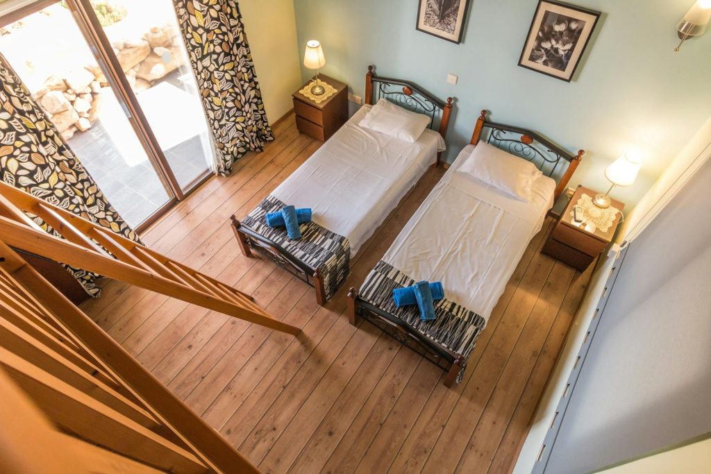 Aerial view of a rustic bedroom with twin beds and wooden decor, featuring a balcony view.
