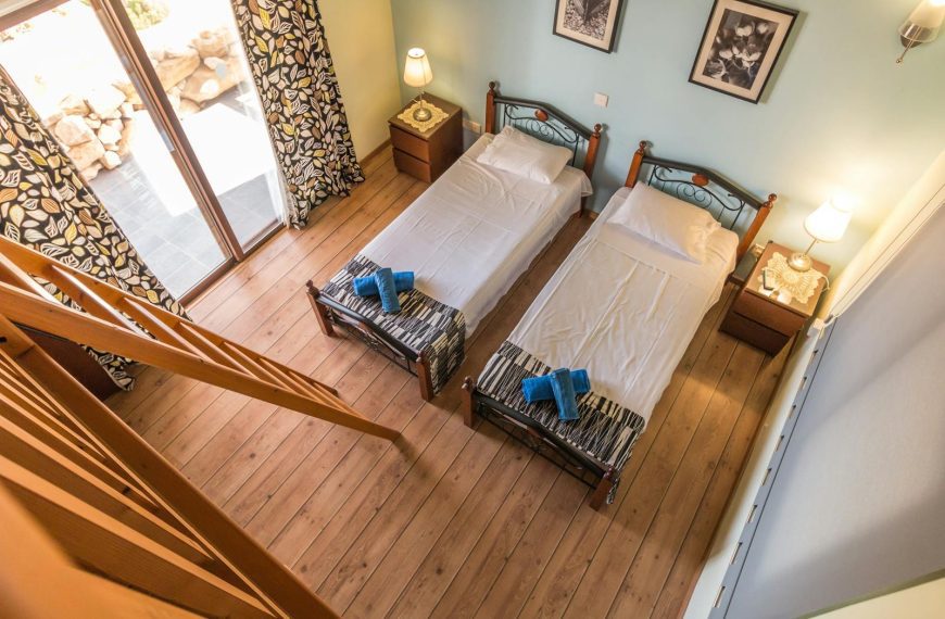 Aerial view of a rustic bedroom with twin beds and wooden decor, featuring a balcony view.