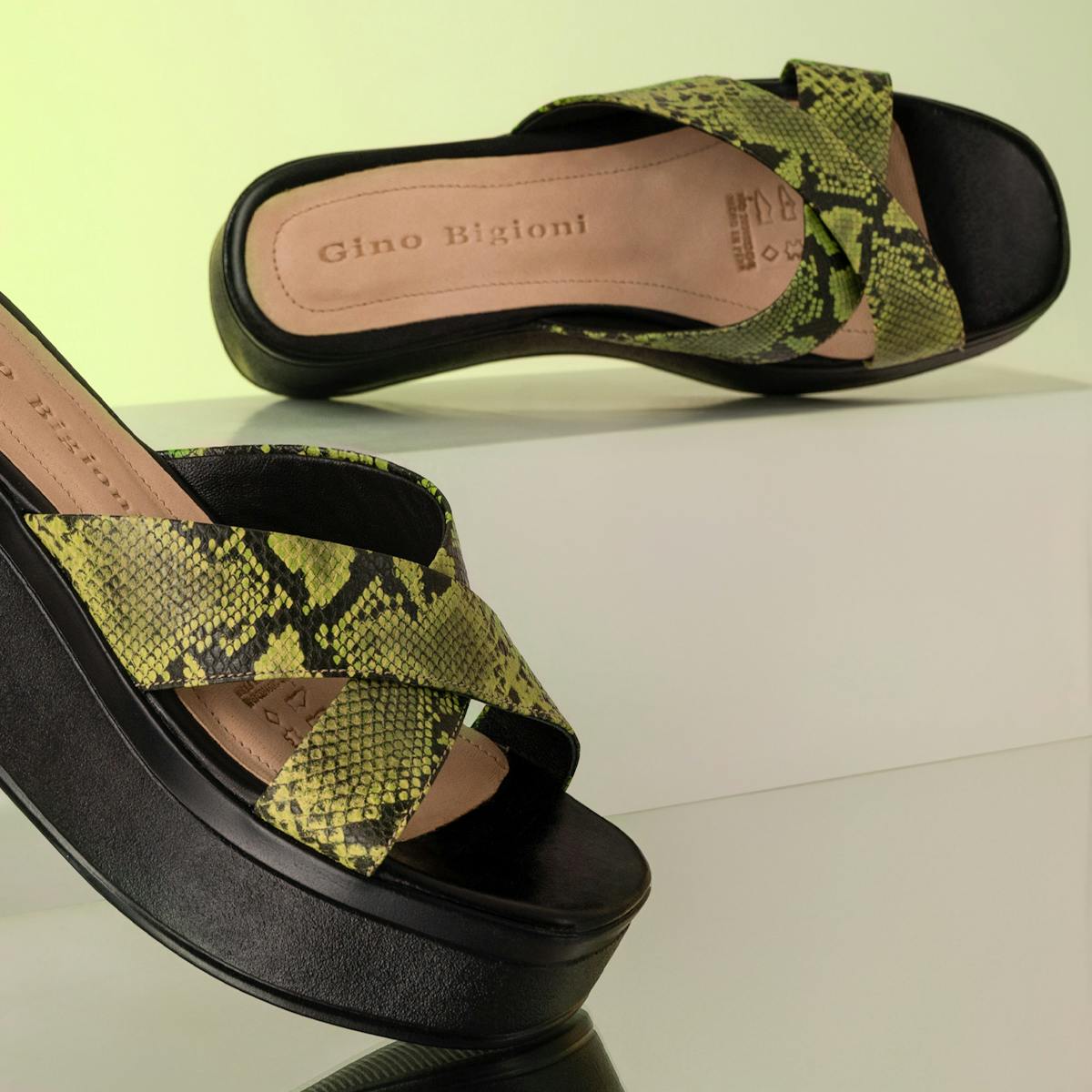 Elegant snake print wedge sandals with cross straps on a minimalist backdrop.