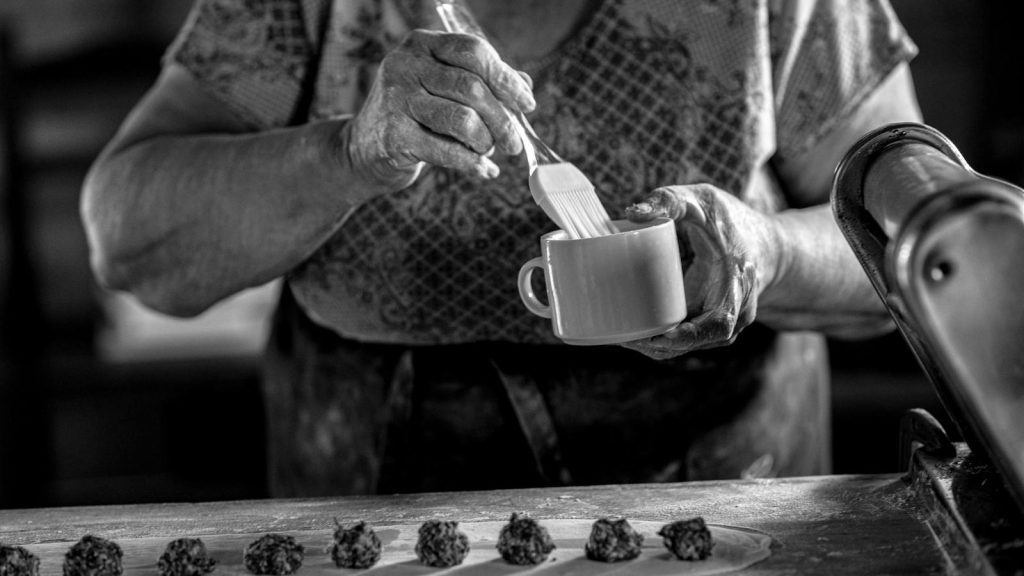 A senior woman prepares homemade pastry in a rustic kitchen setting.