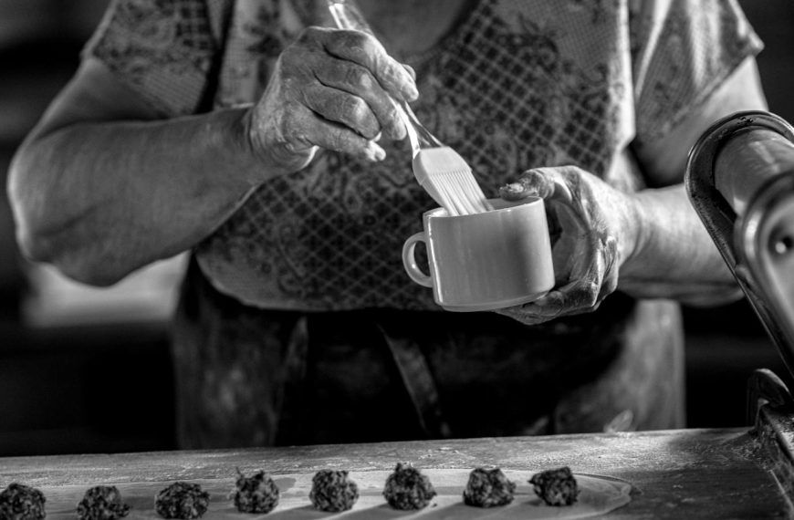 A senior woman prepares homemade pastry in a rustic kitchen setting.