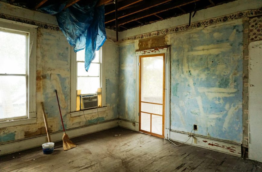 An empty room in an abandoned house with peeling walls and construction tools.