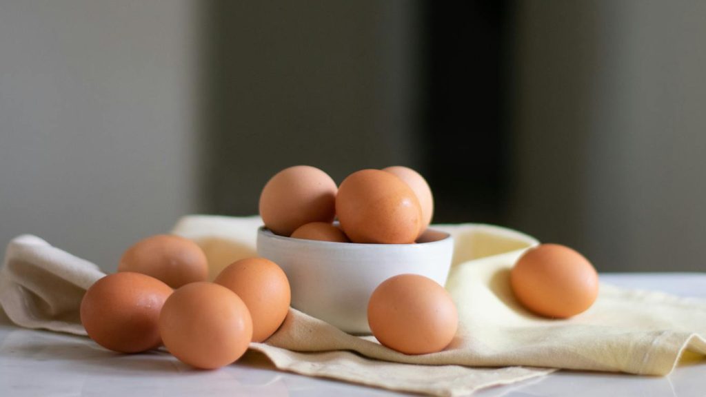 Still life of organic brown eggs in a ceramic bowl on a neutral cloth, showcasing natural textures and a rustic feel.
