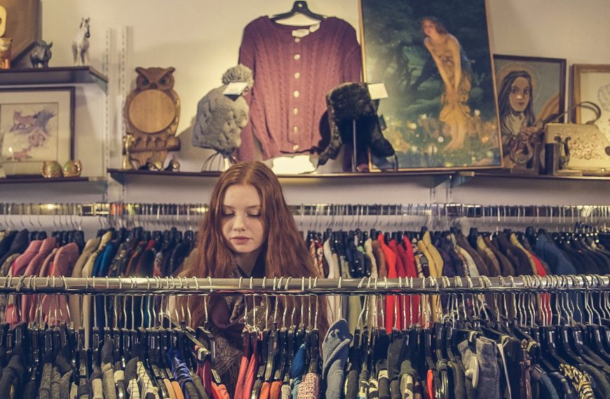A woman explores racks of clothing in a cozy vintage shop with eclectic decor.