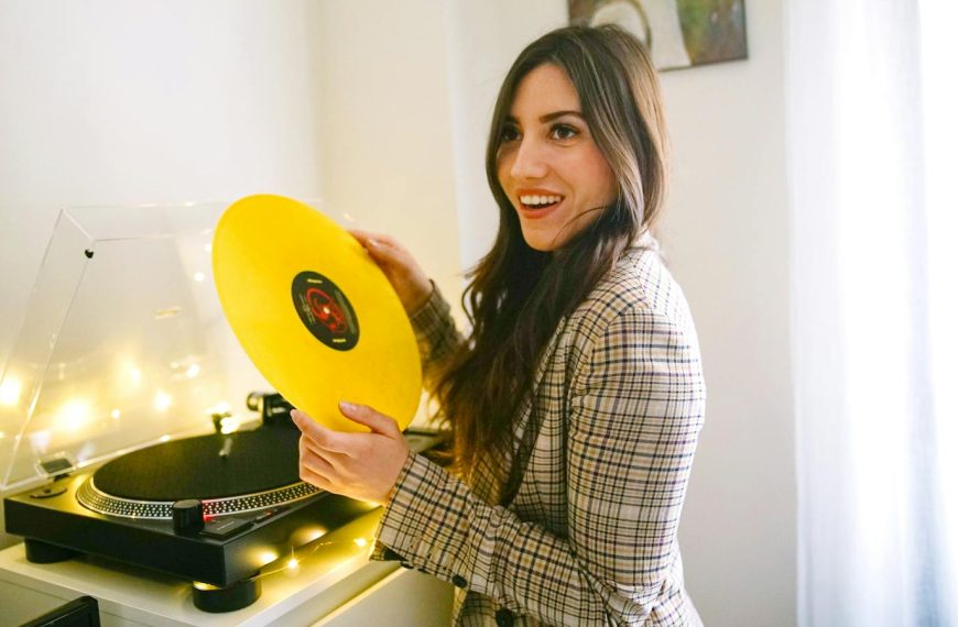 Smiling woman holding a vinyl record indoors, enjoying music.