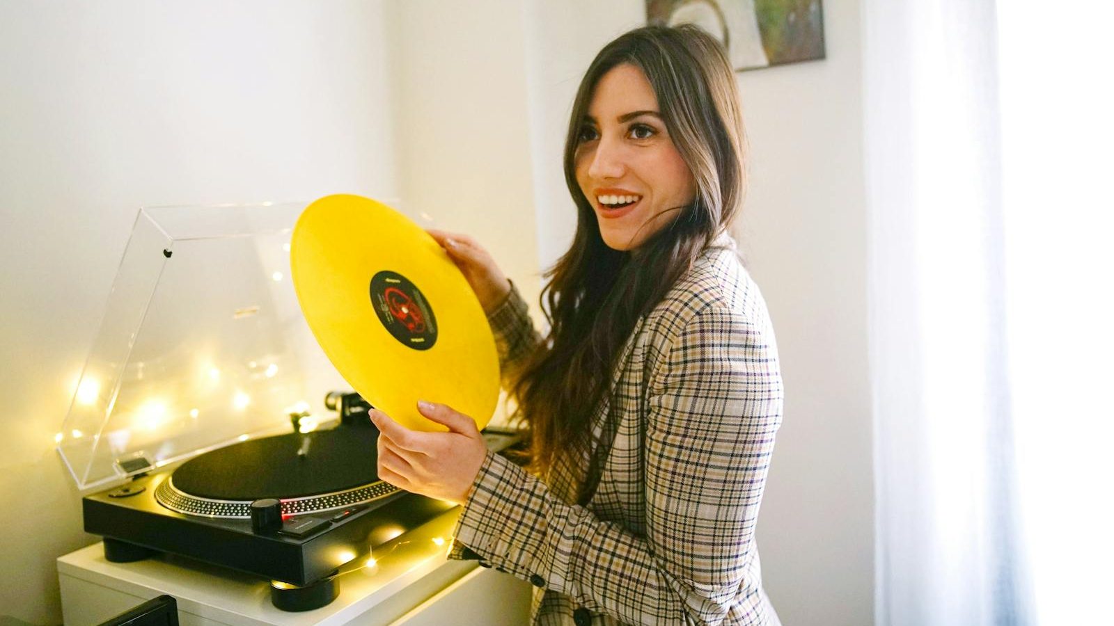 Smiling woman holding a vinyl record indoors, enjoying music.