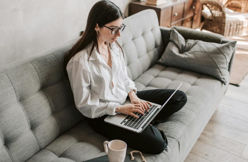 Woman in a cozy home setting working on a laptop for remote work and relaxation.