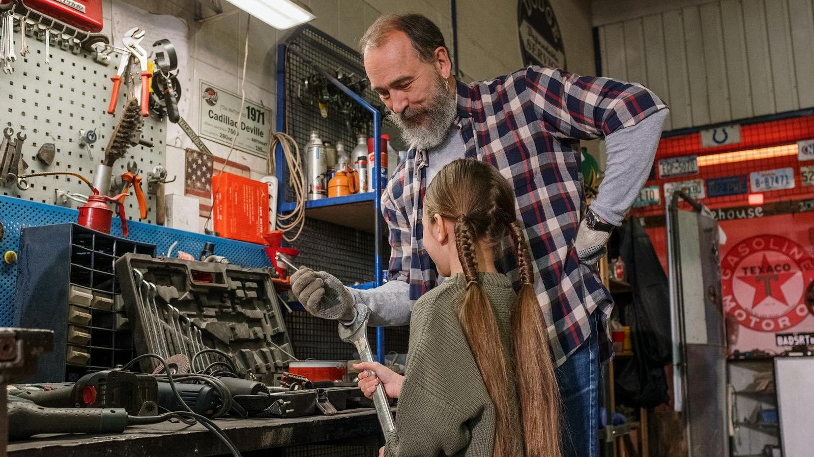 A father and daughter bonding over tools in an auto repair workshop, in a warm family moment.